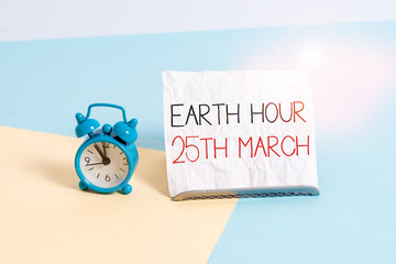 Conceptual hand writing showing Earth Hour 25Th March. Concept meaning symbol commitment to planet Organized World Wide Fund Alarm clock beside a Paper sheet placed on pastel backdrop