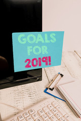 Word writing text Goals For 2019. Business photo showcasing object of demonstratings ambition or effort aim or desired result Note paper taped to black computer screen near keyboard and stationary