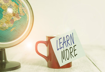Conceptual hand writing showing Learn More. Concept meaning knowledge or skill acquired by instruction Considerable learning Globe map coffee cup sticky note lying vintage wooden table