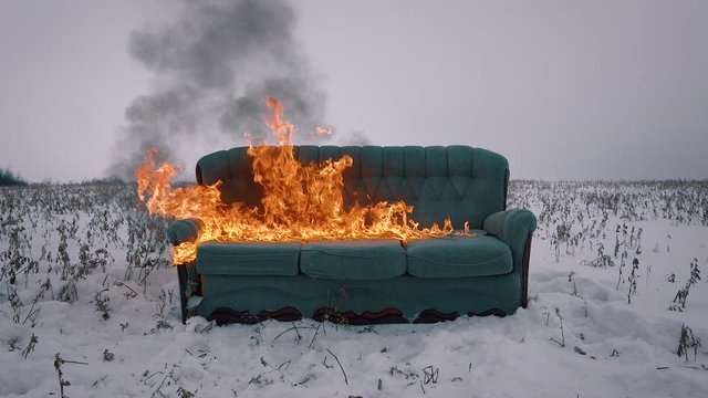 The sofa in the field is flammable. Incineration of furniture. Conceptual video. The concept of destruction, anarchy, disorder, burnout