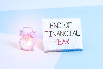 Conceptual hand writing showing End Of Financial Year. Concept meaning Revise and edit accounting sheets from previous year Alarm clock beside a Paper sheet placed on pastel backdrop