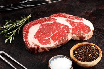 Raw fresh meat Ribeye Steak, seasoning and meat fork on rustic background