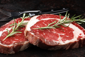 Raw fresh meat Ribeye Steak, seasoning and meat fork on rustic background