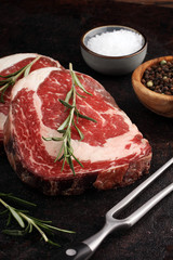 Raw fresh meat Ribeye Steak, seasoning and meat fork on rustic background