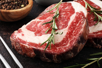 Raw fresh meat Ribeye Steak, seasoning and meat fork on rustic background