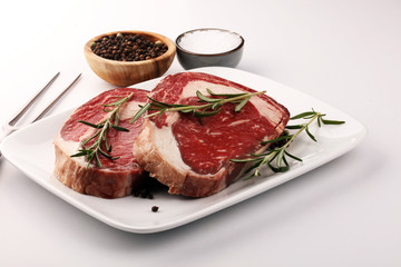 Raw fresh meat Ribeye Steak, seasoning and meat fork on rustic background