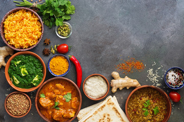 Assorted traditional Indian food on a dark background. Corner frame Indian dish Chicken tikka masala, palak paneer, saffron rice, lentil soup, pita bread and spices. Top view, flat lay,copy space.