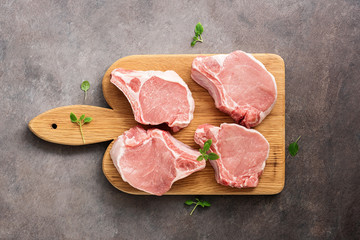 Slices of fresh raw pork on a wooden cutting board, dark rustic background. View from above, flat...