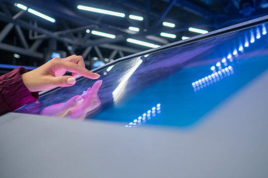 Woman hand using interactive touchscreen display of electronic multimedia terminal at modern technology exhibition. Education, futuristic and technological concept