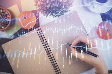 Forex chart hologram on hand taking notes background. Concept of analysis. Double exposure