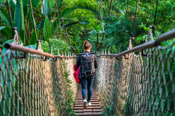 Woman with a backpack walking over a suspension bridge in a jungle