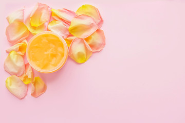 Open jar of cosmetic cream and rose petals on pink background. Concept of organic spa cosmetics. Flat lay, top view, copy space.