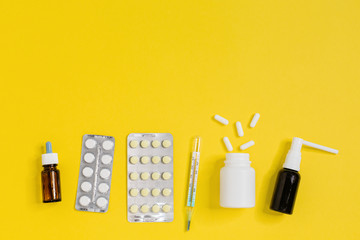 Medicines from home medical kit. Nose drops, pills for flu or cold, thermometer, white pillules from bottle and spray for the throat. Healthcare concept. Yellow background, flat lay, close up.