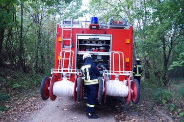Team of German firefighters using a fire-truck in forest, after fire rescue or fire mission....