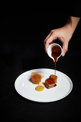 Hand pouring sauce over food on a plate, exquisite dish, creative restaurant meal concept.