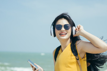 Happy Asian woman with backpack using headphone on the beach, lifestyle concept.