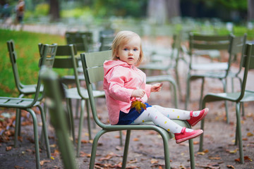 Fototapeta na wymiar Adorable toddler girl sitting on traditional green chair in Tuileries garden in Paris