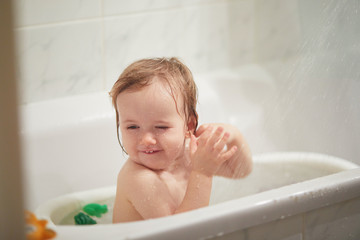 Cute little girl playing in small bathtub