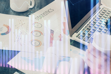 Double exposure of man's hands writing notes with laptop of stock market with forex graph background. Top View. Concept of research and trading.