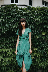 woman wearing an elegant green dress is standing in front of hedge