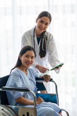 Obraz premium An Asian female doctor cheered on a female patient in a wheelchair in her room.