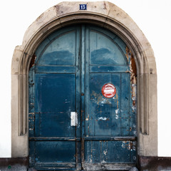 detail view of a large blue arched wooden doorway with a sign in French saying "No Parking in front of Door"