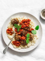 Orzo pasta with meatballs and tomato sauce on light background, top view