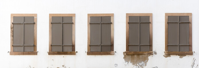 architectural detail of house front with five closed windows with brown shutters