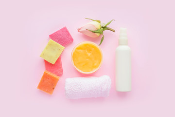 Obraz na płótnie Canvas Open jar of cosmetic cream, white cosmetics bottle, soap, rose and towel on pink background. Concept of natural spa cosmetics. Flat lay, top view, copy space .