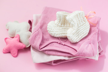 Fototapeta na wymiar Clothes, socks and toys for a newborn girl on a pink background. Motherhood concept