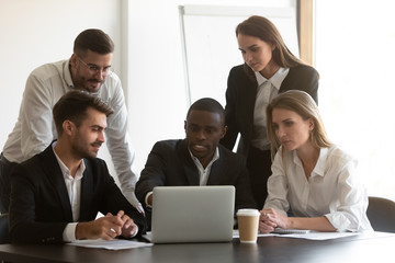 Serious multiracial colleagues discuss project working on laptop