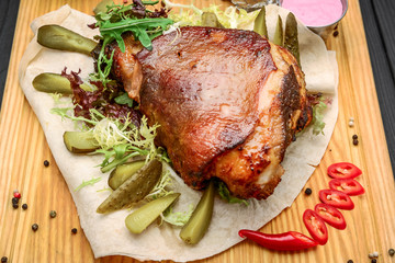 Baked Eisbein with wegetables on wooden board.