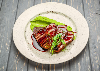 grilled meat with sauce and stewed vegetables on a wooden table
