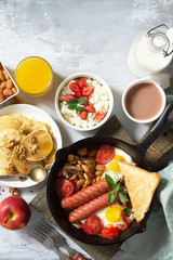Keto breakfast: fried eggs, sausages, beans, bacon, mushrooms, grilled toasts, orange juice, cottage cheese, pancakes and cocoa on a light stone table. Top view flat lay background with copy space.