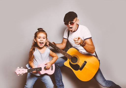 Beautiful little girl playing guitar with her father. Funny lifestyle picture. Happy family timespending. Girl holding pink ukulele ang singing and jumping,