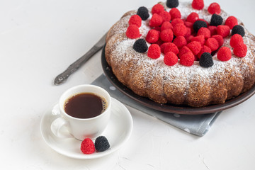 Christmas, holiday cake sprinkled with powdered sugar. Top of raspberry and blackberry. Nearby is a cup of hot coffee. On white background. Copy space. 