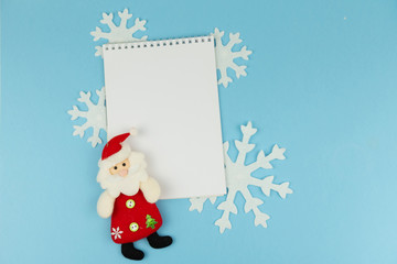 Notebook on blue background with christmas decor. Frame with decorative elements and copyspace on white backdrop. New year goals concept or greeting card concept.