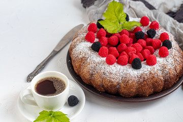 Christmas, holiday cake sprinkled with powdered sugar. Top of raspberry and blackberry. Nearby is a cup of hot coffee. On white background. Copy space. 