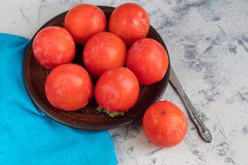 Large, orange persimmon fruits on a brown plate. On a gray, stone background. Copy space. 