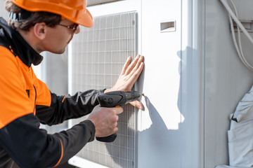 Professional workman in protective clothing installing or reparing outdoor unit of the air...