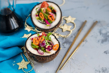 Fresh vegetables salad in coconut peel. Tomatoes, spinach, peppers, chili, radishes. On a gray, stone background. Chopsticks. Copy space. Vegetarian, healthy food. 