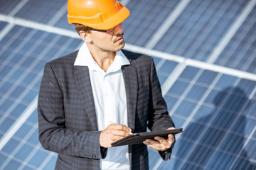 Businessman dressed in the suit with protective helmet working with digital tablet on a solar station. Concept of successful investment in alternative energy