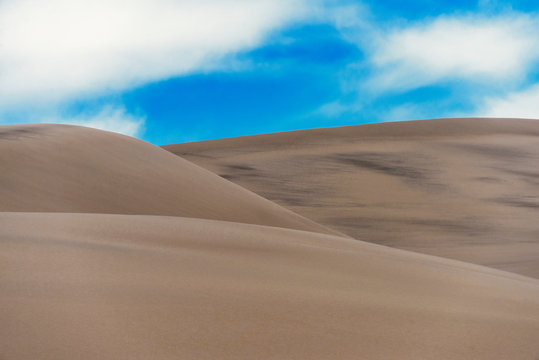 Sand dunes whith dark lines under a cloudy sky. © Oleksiy