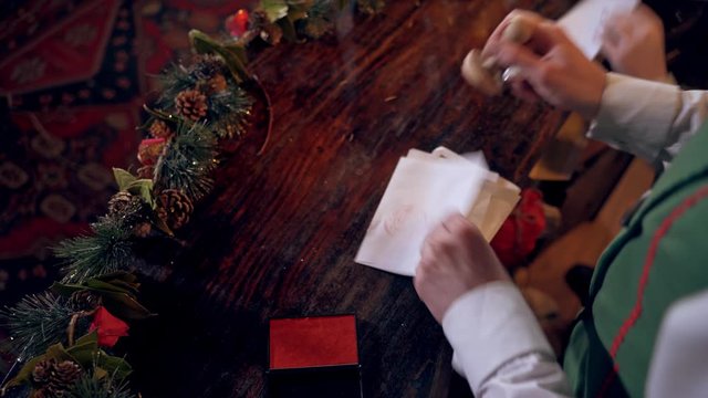 Envelopes for children at Christmas. Elf putting seal on the envelope quickly. Fairy hero making Christmas seal on envelopes.