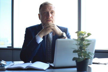 Focused mature businessman deep in thought while sitting at a table in modern office.