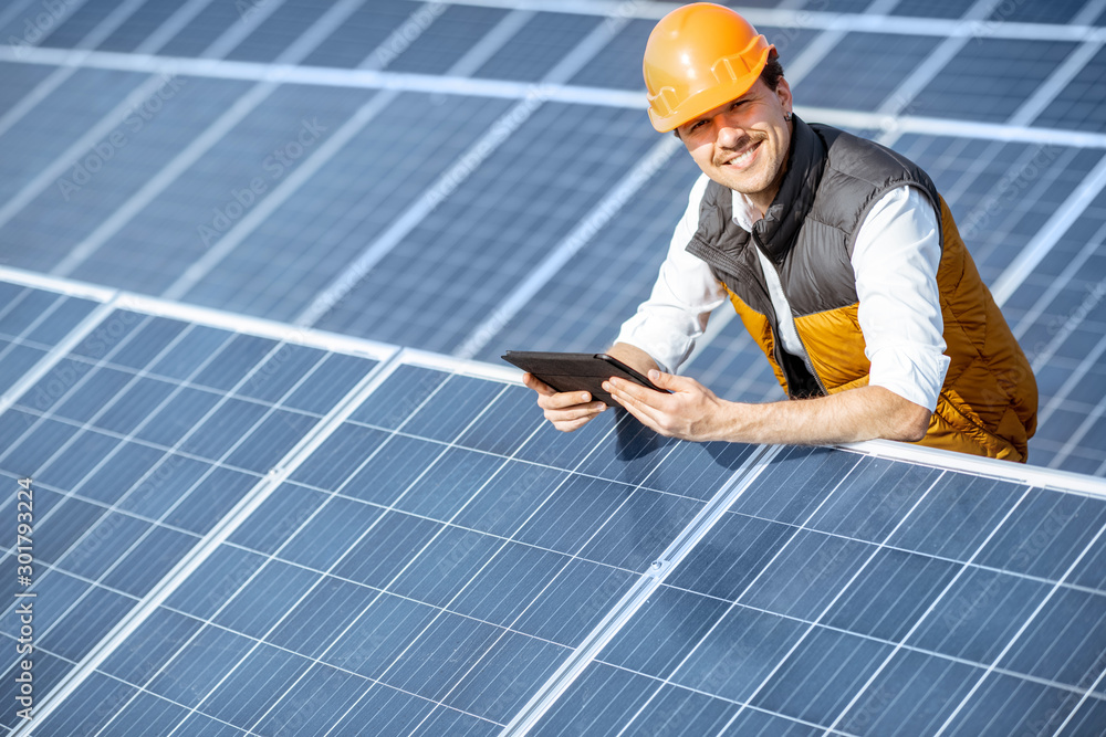 Wall mural portrait of a happy engineer in protective helmet standing with digital tablet on a solar power plan