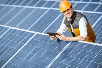 Portrait of a happy engineer in protective helmet standing with digital tablet on a solar power...
