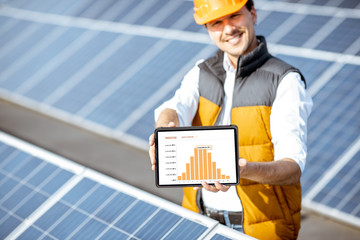 Man showing genaration of solar power plant, holding digital tablet with a chart of electricity...