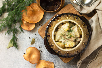Red mushrooms with stewed potatoes, sour cream and spices in a ceramic pot on a stone countertop. Top view flat lay background.