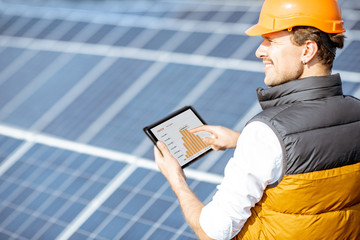 Man examining genaration of solar power plant, holding digital tablet with a chart of electricity production. Concept of online monitoring of the electric station